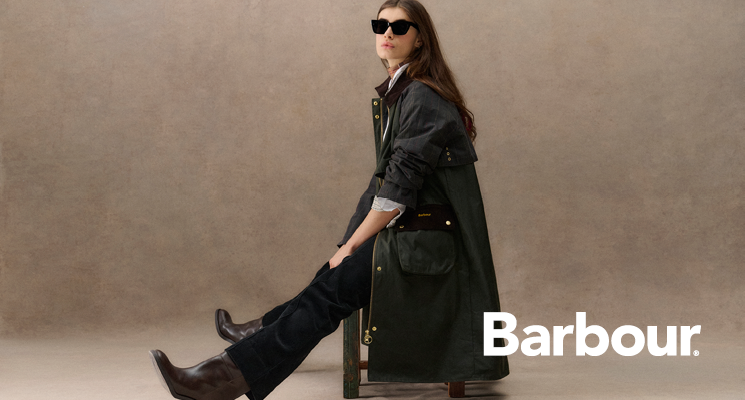 Sitzende Frau mit schwarzem Mantel und schwarzer Hose von Barbour