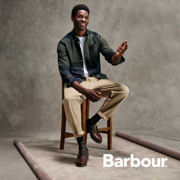 Sitzender Mann mit kariertgrünem Hemd und beiger Hose von Barbour