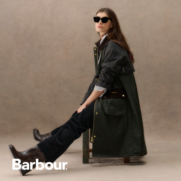 Sitzende Frau mit schwarzem Mantel und schwarzer Hose von Barbour