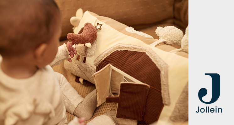 Sitzendes Baby mit weißem Outfit und davorliegendem Spielkissen in creme braun und beige von Jollein