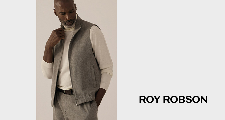 Mann mit grauer Weste und weißem Langarmshirt sowie grauer Stoffhose von Roy Robsen