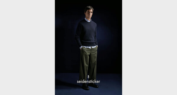 Mann mit dunkelblauem Pullover und blauem Hemd darunter sowie khakifarbener Hose von Seidensticker