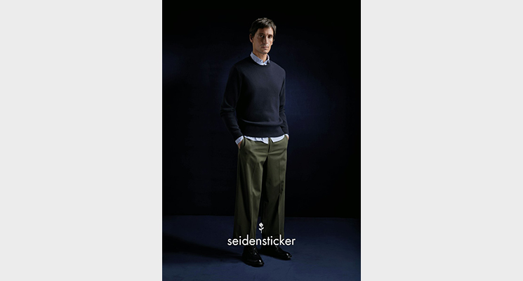 Mann mit dunkelblauem Pullover und blauem Hemd darunter sowie khakifarbener Hose von Seidensticker