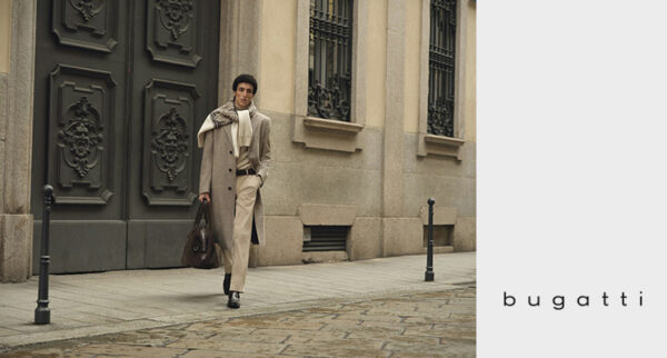Mann mit beigem Mantel, beigem Pullover, beiger Hose sowie um Schulter gebundenem Pullover von Bugatti