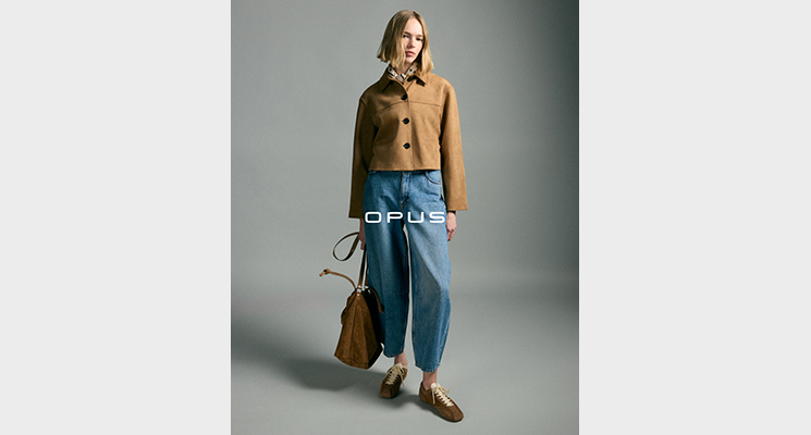 Stehende Frau mit hellbrauner Jacke und blauer Jeans sowie brauner Handtasche von Opus
