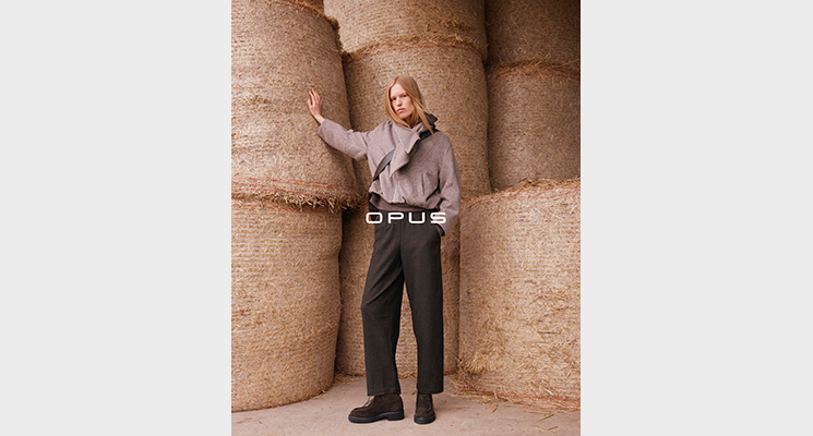 Stehende Frau mit beiger Jacke und brauner Stoffhose und brauner Umhängetasche von Opus