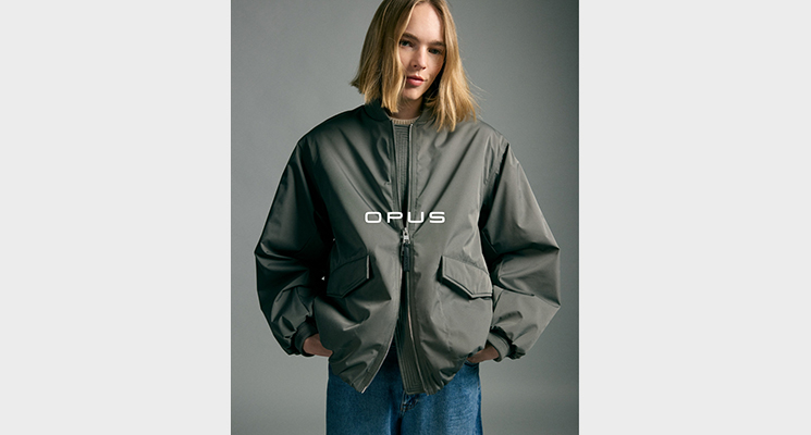 Frau mit Händen in den Hosentaschen die eine khakifarbene glänzende Jacke und eine blaue Jeans von Opus trägt