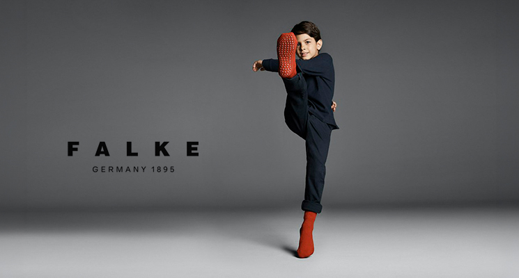 Stehendes Kind welches mit Fuß kickt und rote Stoppersocken von Falke trägt