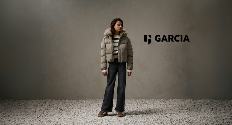 Mädchen in khakifarbener Winterjacke und gestreiftem Pullover sowie blauer Jeans von Garcia