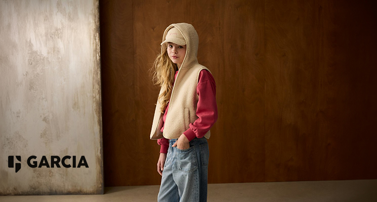Mädchen in beiger Fleeceweste mit Kapuze, rotem Pullover und blauer Jeans von Garcia