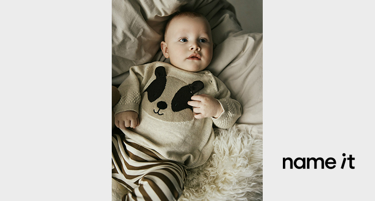 Liegendes Baby in hellem Pulli mit Tiermotiv und gestreifter Hose von Name it