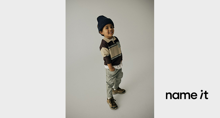 Junge mit gestreiftem Pullover in beige blau und braun sowie hellgrauer Hose und brauner Mütze von Name it