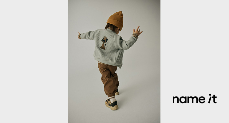 Junge mit hellblauer Fleecejacke mit Hund als Backprint und brauner Hose sowie Mütze von Name it
