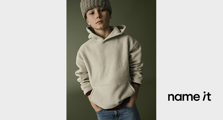 Junge mit naturfarbenem Fleecepullover, Jeans und grüner Mütze von Name it