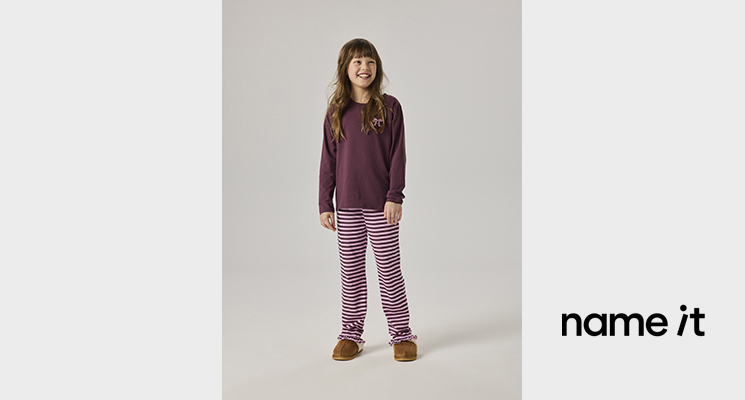 Mädchen in Schlafanzug von Name it mit fliederfarbenem Langarmshirt und weiß flieder gestreiften Hose