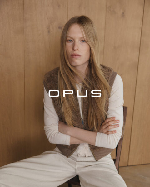 Sitzende Frau mit brauner Fellweste und weißem Langarmshirt sowie brauner Hose von Opus