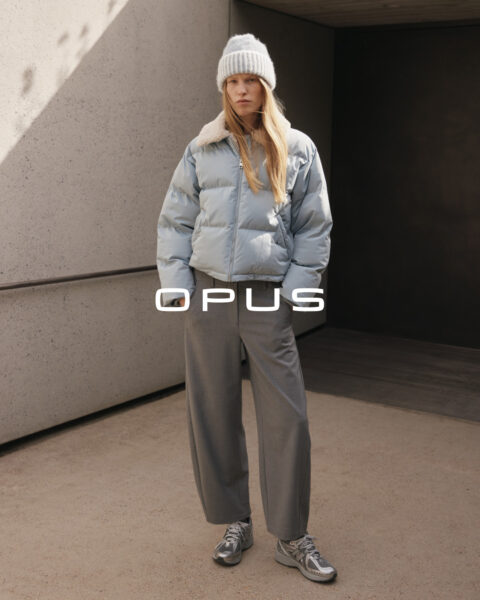 Stehende Frau mit hellblauer Steppwinterjacke und dunkelgrauer Stoffhose sowie hellgrauer Mütze von Opus