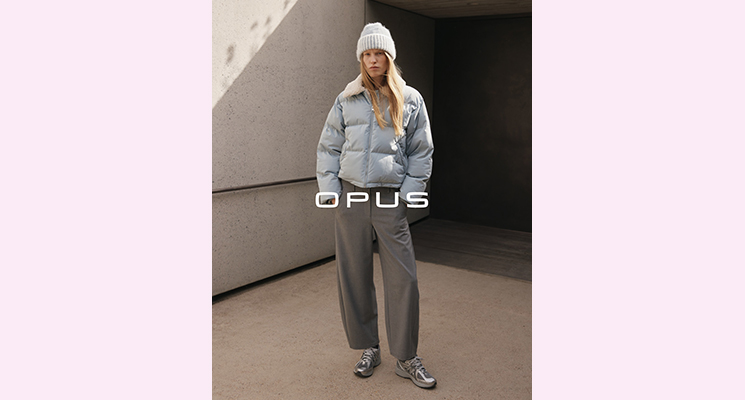 Stehende Frau mit hellblauer Steppwinterjacke und dunkelgrauer Stoffhose sowie hellgrauer Mütze von Opus