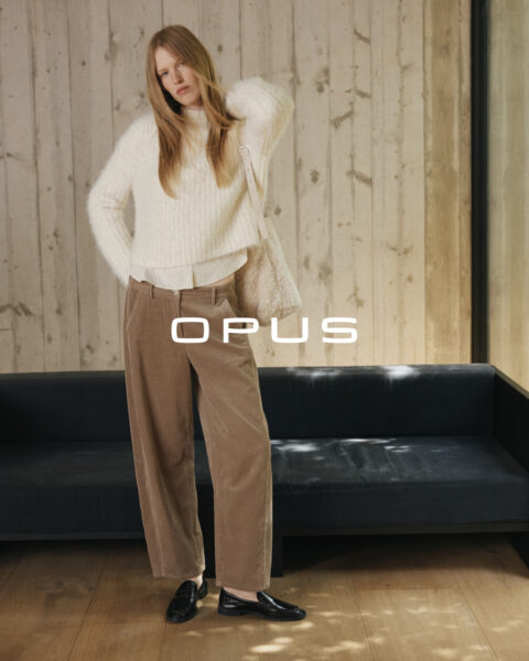 Stehende Frau mit weißem Pullover und weißer Bluse darunter sowie brauner Kordhose von Opus