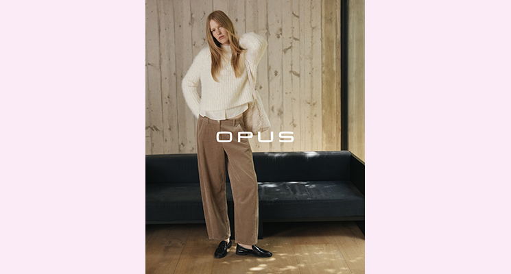 Stehende Frau mit weißem Pullover und weißer Bluse darunter sowie brauner Kordhose von Opus